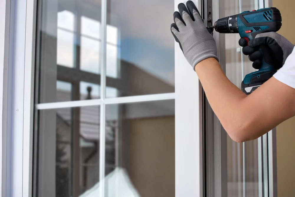 A window installer drilling into the side of a window during an installation.