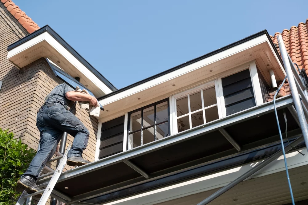 A technician climbing a ladder to a second story window.