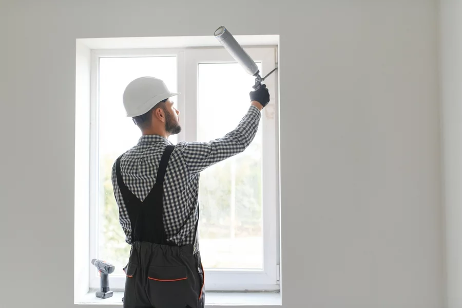 A worker sealing the edges of a window with caulk.